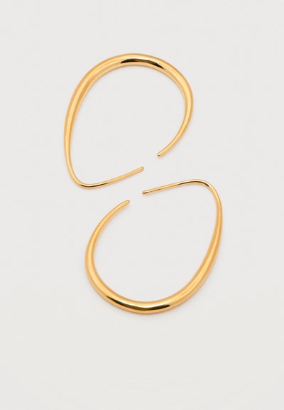 Para cienkich, nieregularnie ukształtowanych złotych kolczyków-kołeczków z delikatnie skręconym wzorem na białym tle.