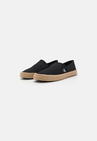 Espadrilles noires en toile avec une semelle en jute tressée et un discret logo sur le côté. Design à enfiler avec un bout arrondi et des accents minimaux.