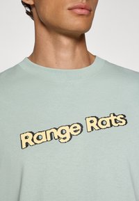 Lys grøn t-skjorte i bomull med teksten "Range Rats" i en retro piksellert font, sentrert på brystet i gul med svarte konturer.