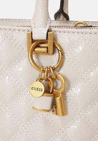 Hvid quiltet håndtaske lavet af glansfuldt materiale med guld hardware, en nøglecharme og en lille hængelås med "GUESS"-logo.