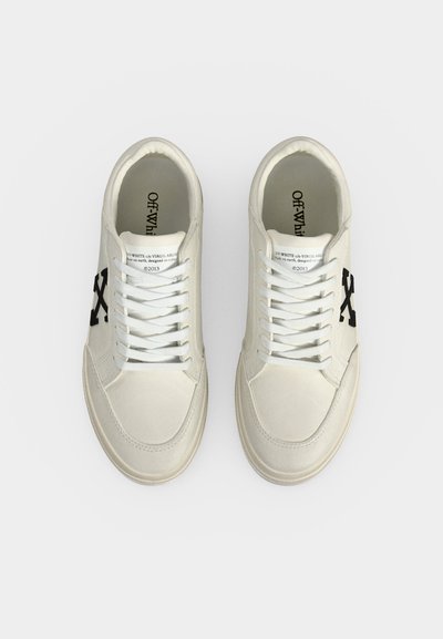 Ζεύγος λευκών χαμηλών sneakers με μαύρο λογότυπο "X" στις πλευρές, λευκά κορδόνια και κείμενο στη γλώσσα και στη σόλα με την επιγραφή "Off-White".