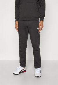 Sort sweatshirt med kængurulomme, sammensat med mørke sweatpants med sidelommer, begge lavet af blødt stof. Hvide logoaccente.