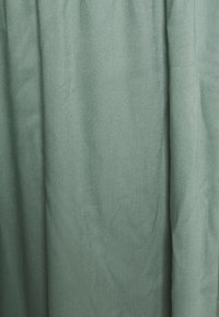 Rideau en tissu lisse et texturé de couleur vert atténué. Présente des plis doux et un design simple, sans motifs ni embellissements visibles.