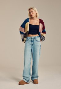 Knitted multicolored cardigan, black cropped top, light blue baggy jeans, and brown platform slip-on shoes. Smooth textures and loose fit.
