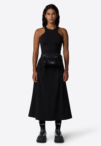 Svart ärmlös topp i kombination med en lång svart kjol, med en liten svart midjeväska, svarta strumpor och grå sportskor. Enkelt design.