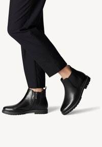 Black leather ankle boots with elastic side panels and zip closure. Treaded rubber sole. Worn with black tapered pants.
