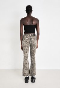 Jean évasé imprimé léopard dans des tons de beige et de brun, avec une taille haute, une coupe slim et une texture légèrement usée, associé à des chaussures noires.