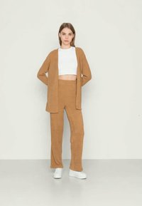 Cardigã de malha bege combinado com calças largas a condizer; top crop branco; textura suave; corte descontraído; design simples; usado com ténis brancos.