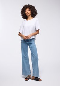 Top corto bianco e strutturato a maniche corte, abbinato a jeans a gamba larga azzurri e sandali neri con borchie. Outfit semplice e casual con una vestibilità ampia.