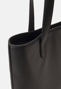 Sac fourre-tout en cuir noir avec une texture lisse, une forme allongée et deux poignées robustes ; présente un design simple et minimaliste.