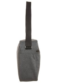 Šedá látková taška s plochým dnem, širokým černým popruhem a bočním zipovým kapsou pro další úložný prostor. Jednoduchý, funkční design.