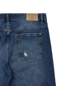 Jeans en denim de lavage bleu foncé avec une poche usée, une étiquette en cuir marron à la taille et des détails de couture contrastés.