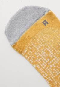 Chaussette jaune avec un revers gris, arborant un motif texturé avec des points. Petite étiquette grise avec un "R" sur le revers. Matériau doux et tricoté.