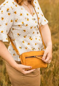 Žlutá kožená crossbody taška s přední kapsou na zip, hladkým povrchem, obdélníkovým tvarem a nastavitelným popruhem.