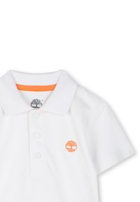 Witte poloshirt met korte mouwen, voorzien van een drieknopen sluiting. Een oranje boom logo is geborduurd op de linkerborst. Getextureerde stof.