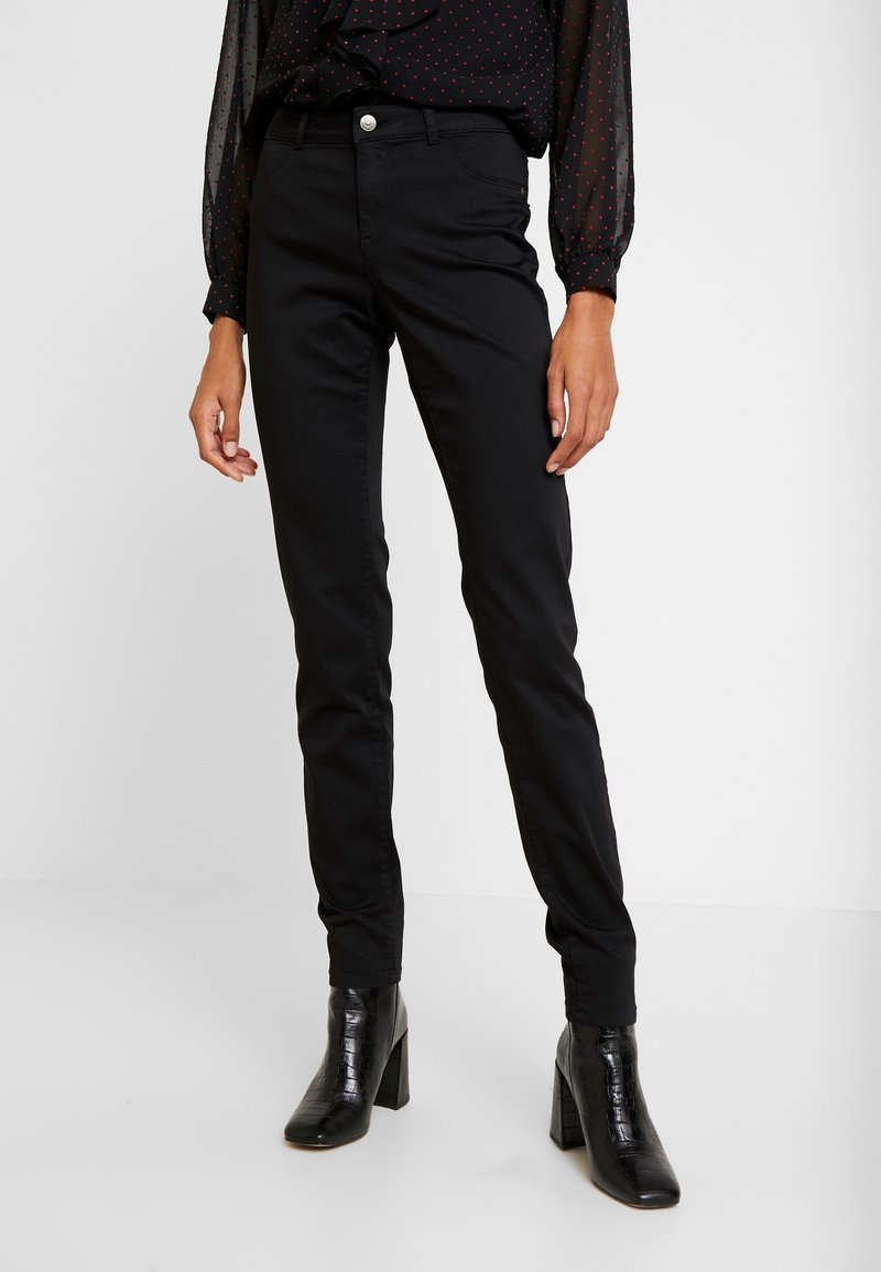 Black fitted pants made of soft fabric, featuring a classic five-pocket design, front button closure, and straight legs. Worn with heeled boots.