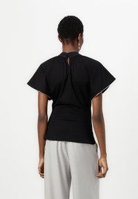 Black top with short, wide sleeves, a high neck, and a button closure at the back. Pairing with light gray tailored trousers.