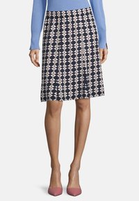 Laivastonsininen hame, jossa on valkoisia ja vaaleanpunaisia geometrisia kuvioita, pliseerattu design ja joustava vyötärönauha, yhdistettynä vaaleanpunaisiin teräviin korkokenkiin.