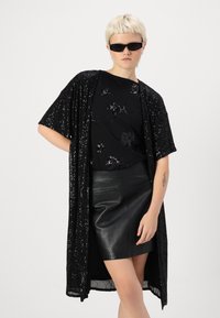 Černý sequinový kimono cardigan s krátkými rukávy přes černé tričko s jemným květinovým vzorem a těsnou černou koženou sukni.