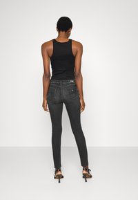 Jeans ajustados negros con una cintura de talle medio, bolsillos traseros y detalles de costura sutiles. Combinados con una blusa sin mangas negra y tacones.