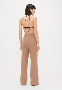 Καφέ πλεκτό παντελόνι σε φαρδιά γραμμή με υφή κα�ι ψηλή μέση με λεπτομέρεια κουμπιού, συνδυασμένο με ένα μαύρο μπικίνι με λαιμόκοψη.