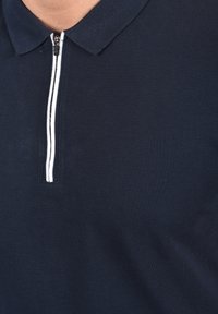 Marine polo skjorte med kort glidelås, med en hvit vertikal stripe langs glidelåsen for kontrast. Teksturert stoff med klassisk krage.