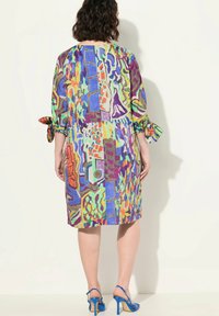 Värikäs mekko, jossa on sekoitus geometrisia ja abstrakteja kuvioita purppurassa, sinisessä, vihreässä ja oranssissa, rullauslaskelmilla ja rento istuvuus.