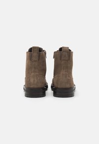 Brązowe zamszowe botki za kostkę o gładkiej fakturze, czarna gumowa podeszwa, z tyłu zamki błyskawiczne i pętelka na obcasie.