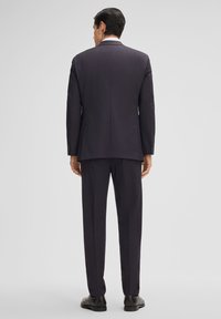 Marineblauwe blazer met notch revers, enkele ventilatie en een getailleerde pasvorm, gecombineerd met bijpassende broek en zwarte leren schoenen, gezien vanuit de achterkant.