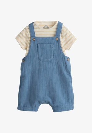 Bež košulja s kratkim rukavima s prugama uparena s plavim pamučnim kombinezonom za bebe koji ima prednji džep i drvene kopče na dugmad.