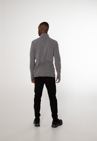 Grå langærmet top med høj hals, parret med sorte bukser. Stoffet ser blødt og ribbet ud, med et afslappet design.