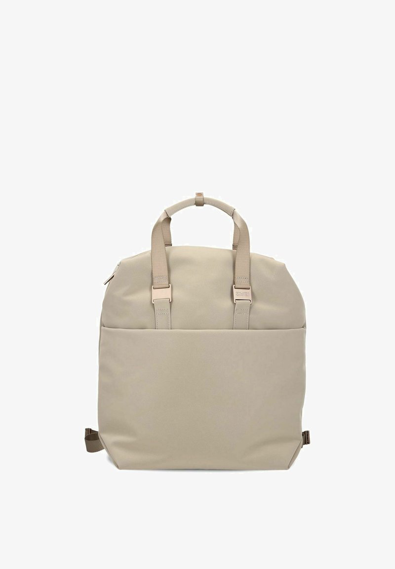 Zaino beige con una texture liscia, dotato di due manici, spallacci regolabili e una tasca con cerniera. Design semplice e minimalista.