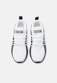 Λευκά υφασμάτινα αθλητικά παπούτσια με μαύρες λεπτομέρειες, διαθέτουν επάνω μέρος από δίχτυ, εντυπωσιακό σύστημα κορδονιών και τη σήμανση "VERSACE JEANS COUTURE" στη γλώσσα.