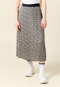 Jupe plissée navy à motif floral, avec taille élastique et design mi-long, assortie à des baskets blanches et des chaussettes à rayures multicolores.