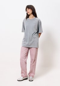 Graues Baumwoll-T-Shirt mit kurzen Ärmeln und Rundhalsausschnitt, kombiniert mit hellrosa strukturierten Hosen und silbernen Slippern.