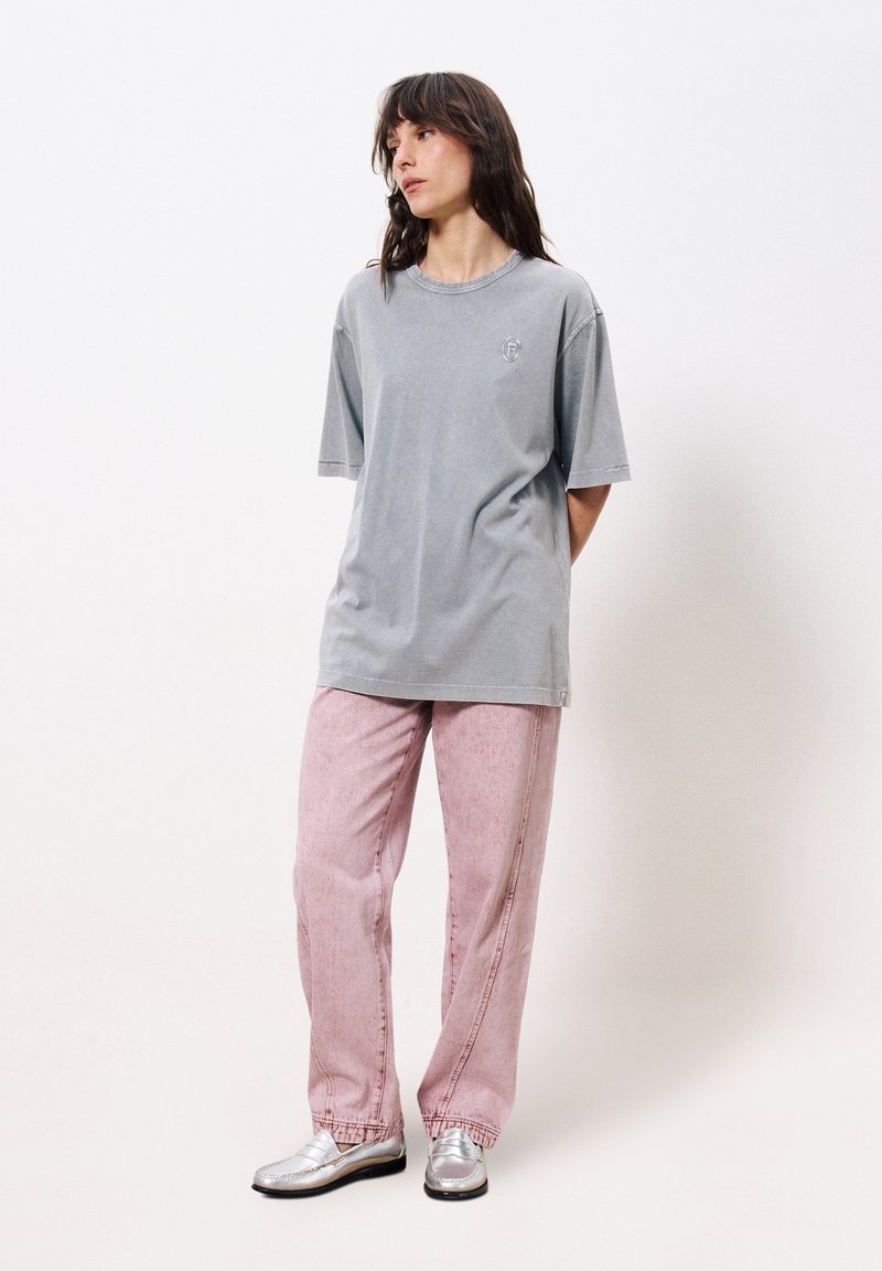 Graues Baumwoll-T-Shirt mit kurzen Ärmeln und Rundhalsausschnitt, kombiniert mit hellrosa strukturierten Hosen und silbernen Slippern.