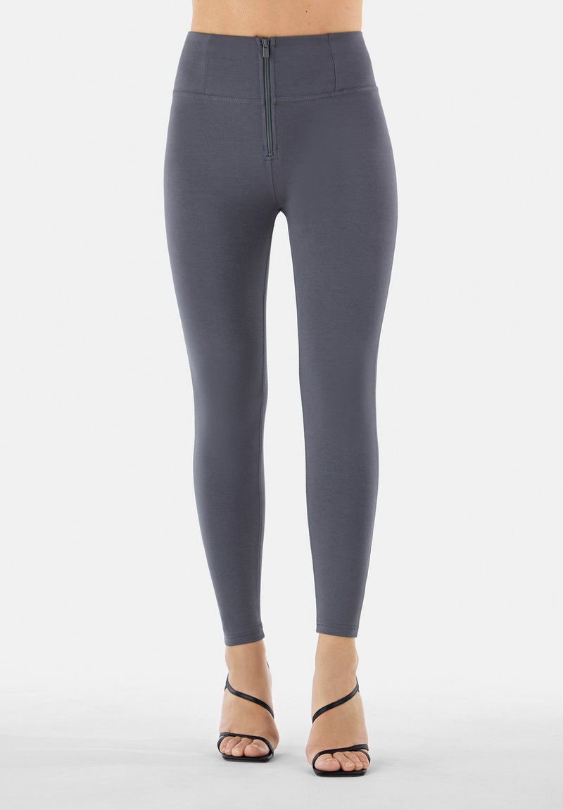 Leggings grigi a vita alta con una zip frontale, realizzati in un materiale liscio e elasticizzato che si adatta alle gambe.