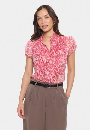 Pink floral blouse with ruffled neckline and short sleeves, featuring a light, sheer fabric. Paired with high-waisted brown trousers and a black belt.