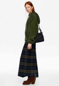 Zielona, puszysta kurtka z kapturem, długa spódnica w krat�ę w ciemnoniebieskim i zielonym kolorze, brązowe zamszowe botki na grubym obcasie oraz czarna torebka z zamkami błyskawicznymi.