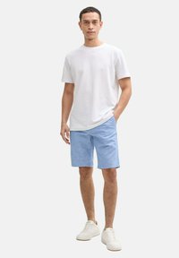 Camiseta de algodón blanca de cuello redondo, pantalones cortos azul claro y zapatillas blancas. El conjunto presenta un corte relajado y un estilo casual.