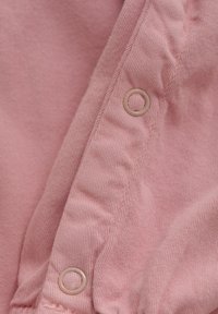 Rosa Stoff mit einer weichen Textur, der sichtbare Nähte und ein rundes Knopfloch in heller Farbe aufweist, alles auf einem gefalteten Kleidungsstück.