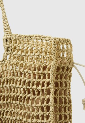 Vävd halmmugg med en stor öppen design, med ett beige tyginteriör. Remmen är också vävd vilket kompletterar väskans naturliga utseende.