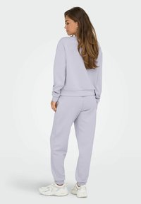 Sudadera de color púrpura claro y joggers a juego, confeccionados en tejido suave, con puños acanalados y cinturilla elástica, combinados con zapatillas blancas.