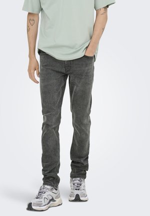 Jean en denim gris à coupe droite, associé à un t-shirt vert clair et des baskets de sport grises. Design simple avec des accents minimes.