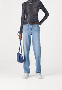 Jeans de mezclilla azul con un corte recto, lavado claro y bolsillos frontales. Combinados con una blusa de manga larga con estampado de serpiente y un pequeño bolso azul.
