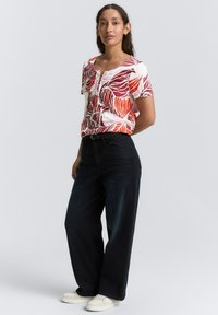 Haut à manches courtes floral avec des motifs de feuilles rouges et oranges, associé à un jean large bleu marine et des baskets blanches.