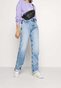 Ljusblå vida jeans, kombinerade med en lavendelfärgad sweatshirt och en svart midjeväska. Vita sneakers med neonaccentuerade detaljer fulländar looken.