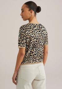 Pull à manches courtes imprimé léopard en beige et noir, avec un col et un ourlet côtelés. Le tissu a une apparence tricotée texturée.