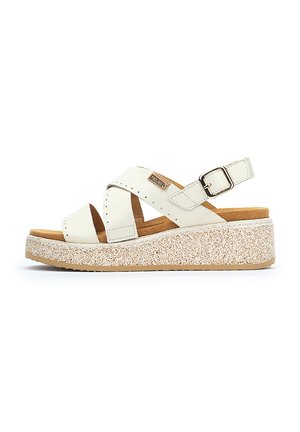 Sandales en cuir blanc avec des brides croisées, une boucle et une semelle plateforme mouchetée. La semelle intérieure est marron et texturée pour le confort.