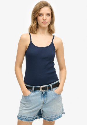 Granatowy prążkowany top na ramiączkach z cienkimi paskami, połączony z jasnoniebieskimi szortami dżinsowymi z postrzępionymi brzegami oraz czarnym paskiem z srebrną klamrą.